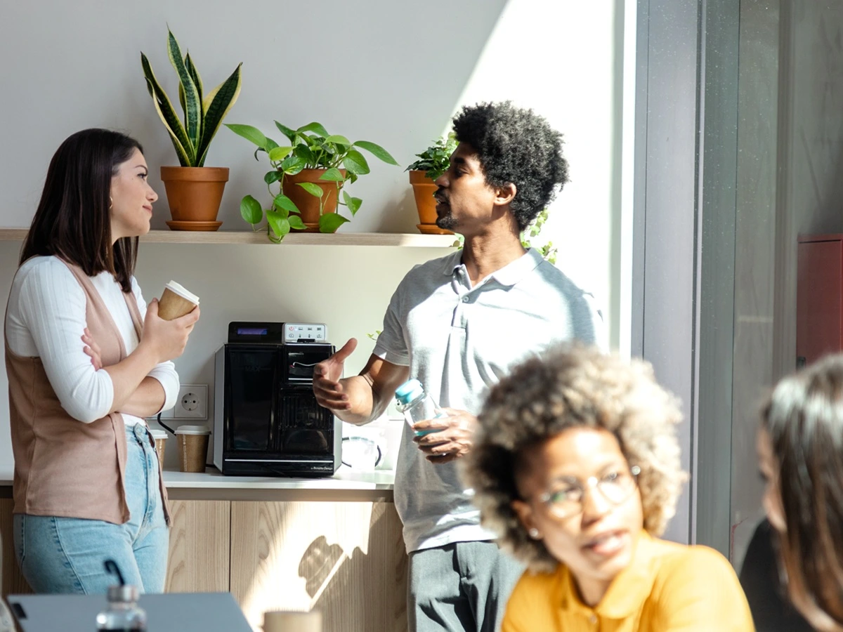 Two coworkers having a coffee break and chat while colleagues keep working. Coffee break concept.