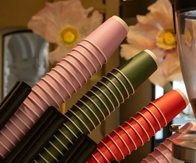 Stack of coloured compostable paper coffee cups displayed beside a commercial coffee machine